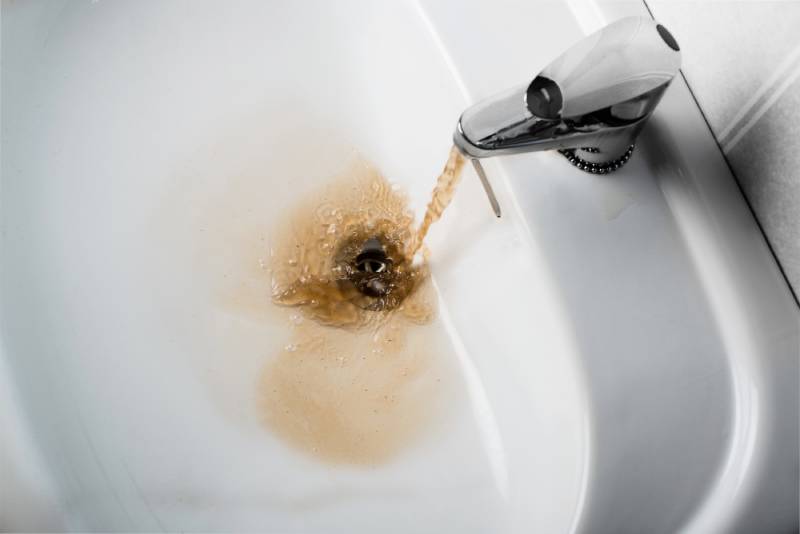 Rusty water flowing from faucet into sink.