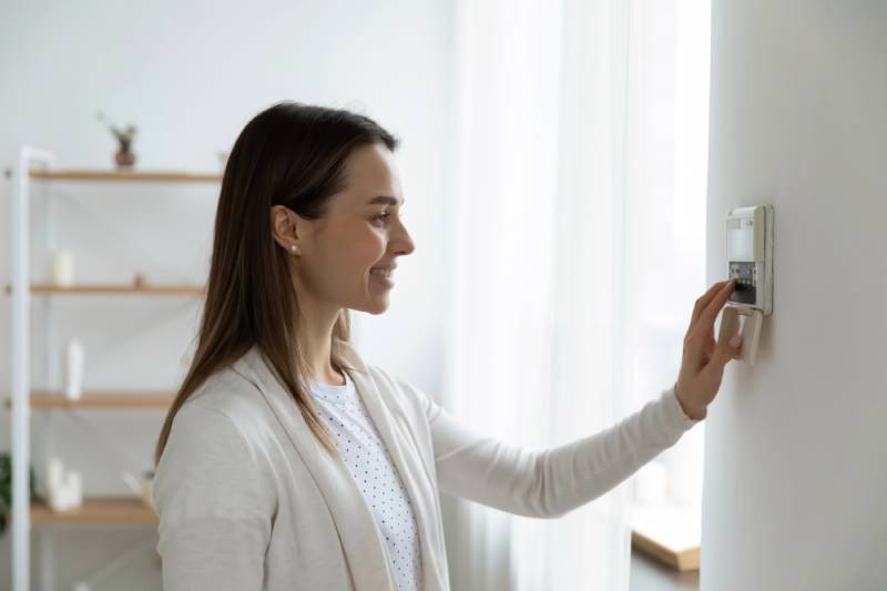 Woman adjusting digital thermostat at home