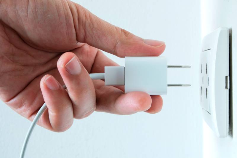 Hand plugging charger into wall outlet