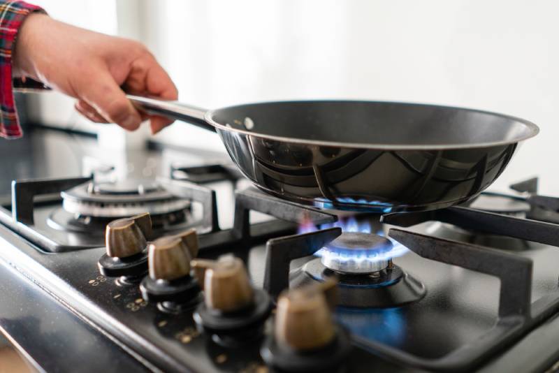 Hand holding frying pan over lit gas burner.