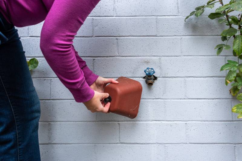 Person in purple shirt placing cover on outdoor faucet