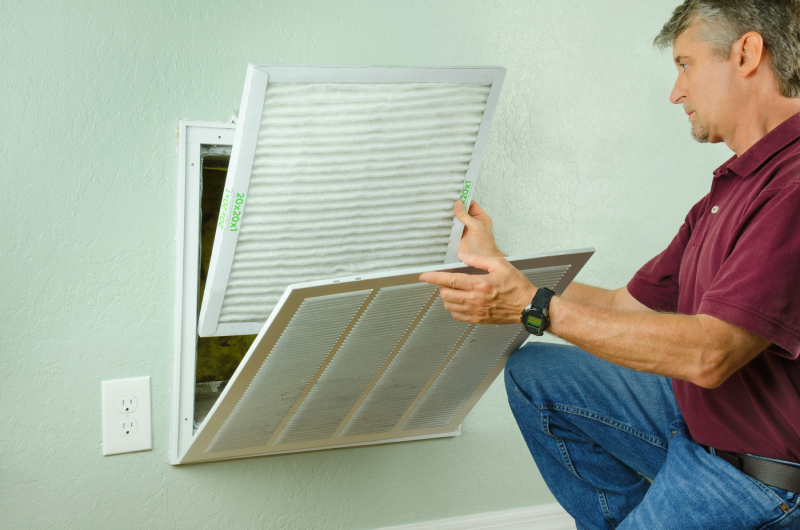 Man replacing HVAC filter in wall vent.
