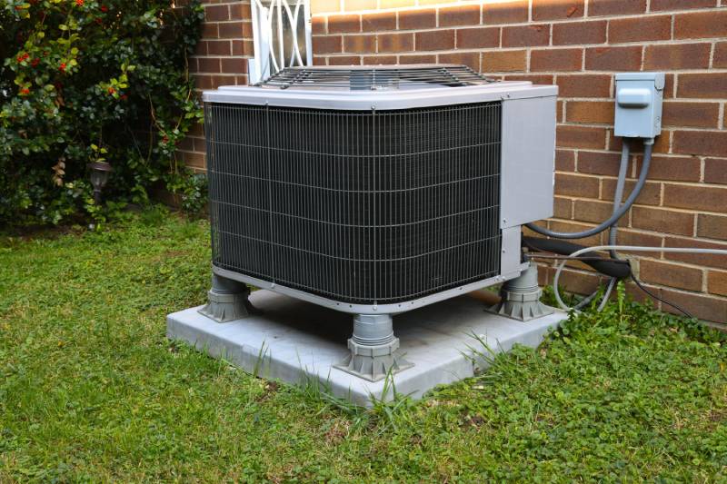 Outside AC unit on concrete pad by brick wall