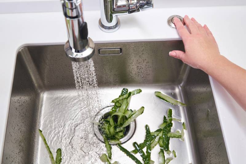 Hand operating sink disposal with cucumber peels.