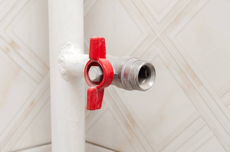 Red valve on pipe against tiled wall