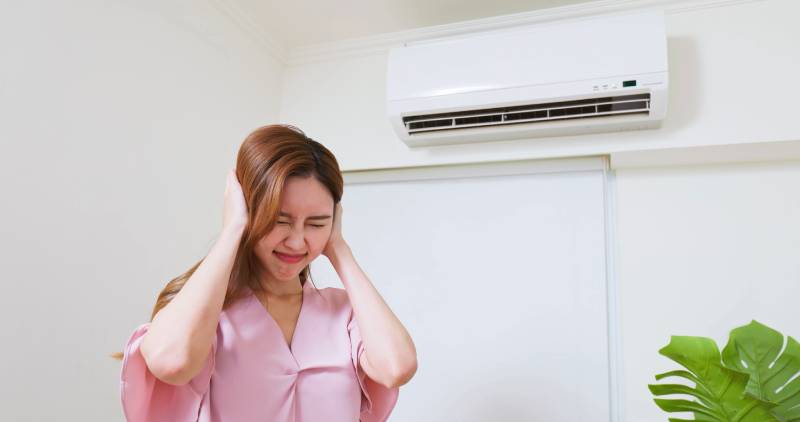 Woman covering ears near noisy air conditioner.
