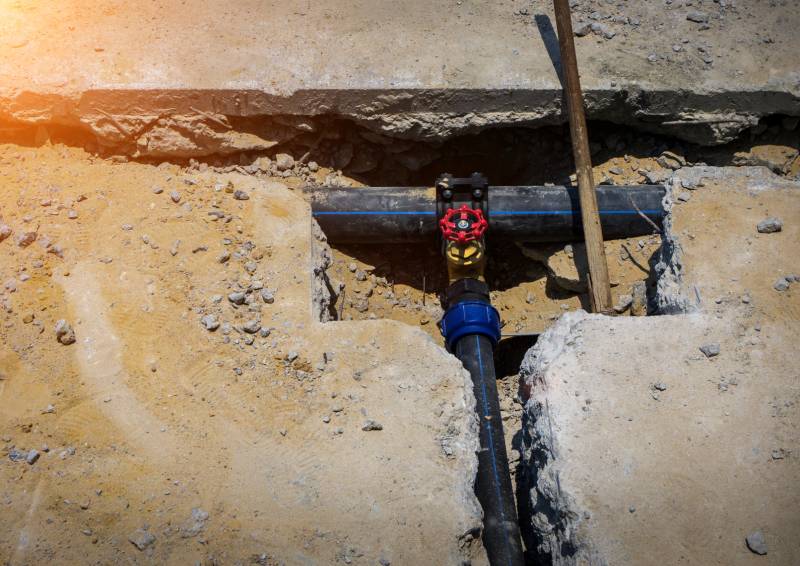 Underground sewer pipe with valve exposed in trench.