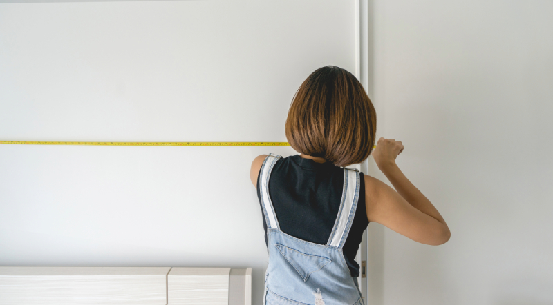 Person measuring wall with tape measure.