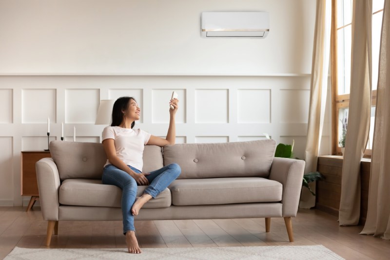 Woman adjusting wall-mounted AC with remote.