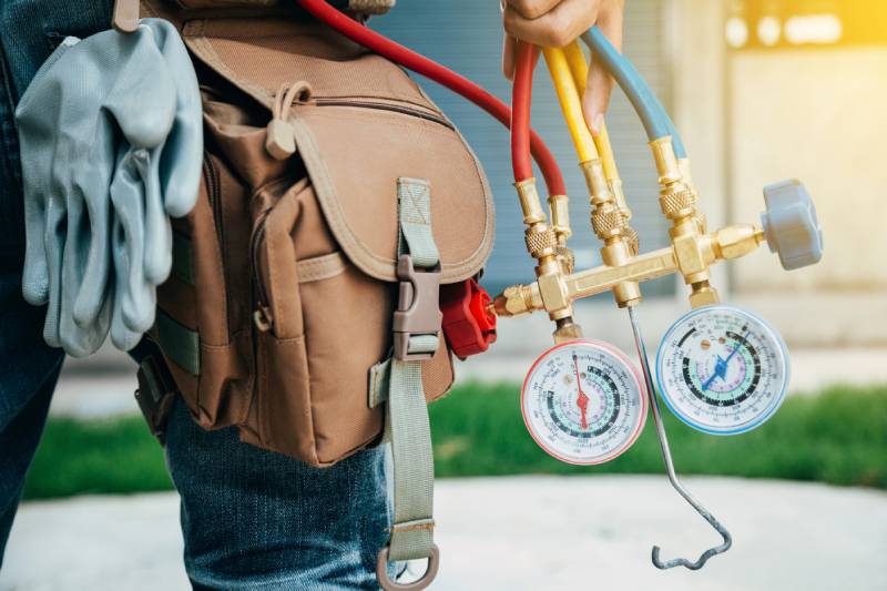 HVAC technician holding gauges and tool bag.