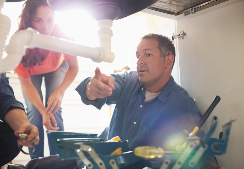 Man examining plumbing under sink.