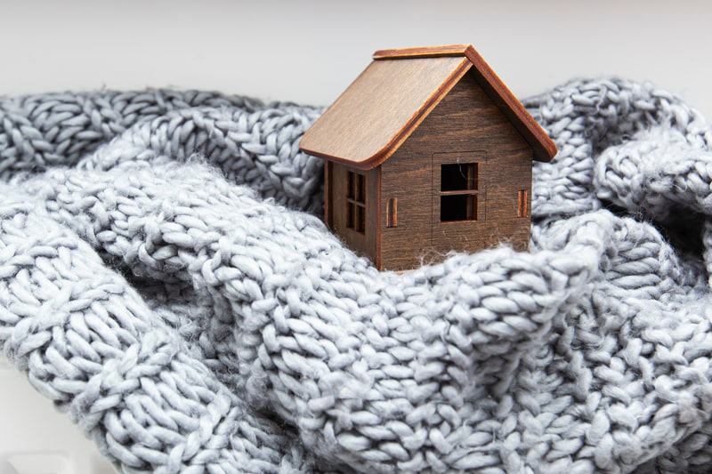 Wooden house wrapped in gray knit blanket.