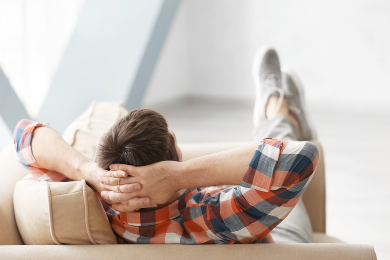 Man relaxing on couch, hands behind head