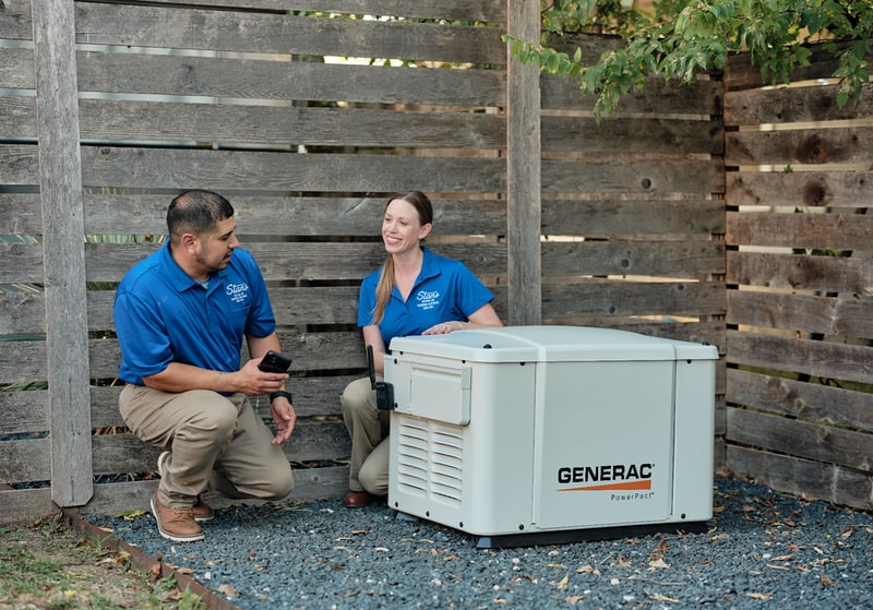 Two technicians in blue shirts beside a Generac home generator.