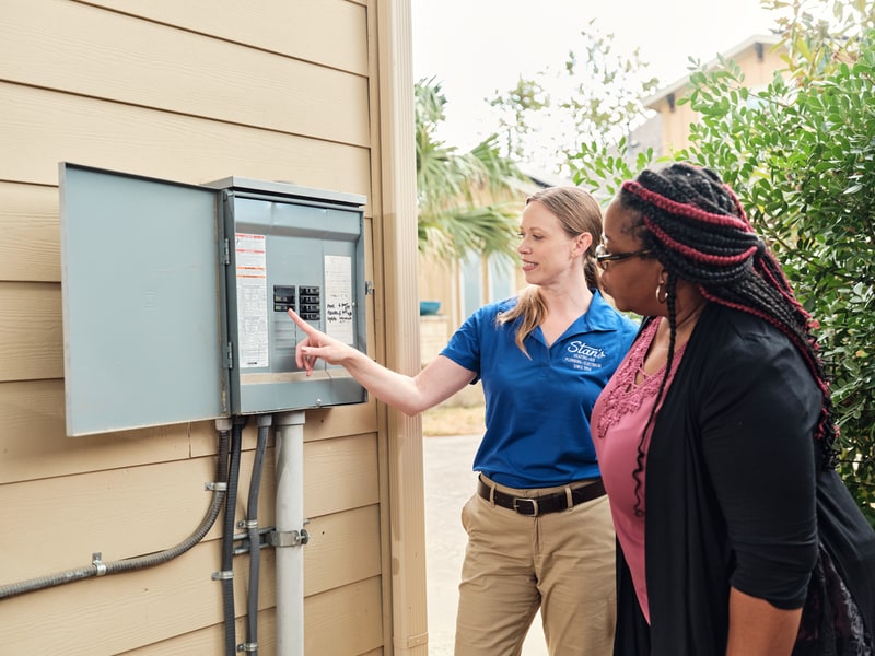 A technician showing a woman a breaker box outside a house.