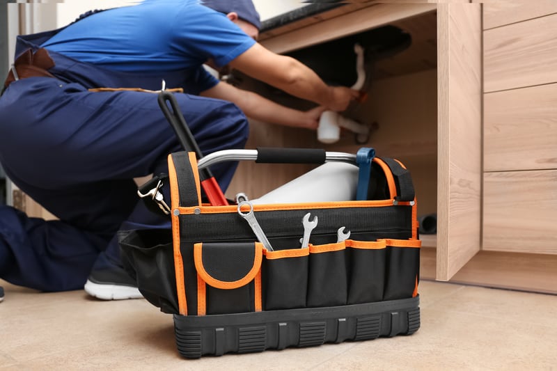 Plumber working under sink with toolkit nearby.