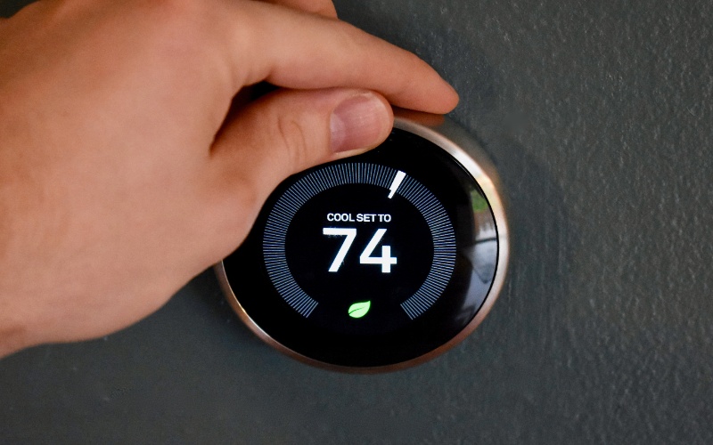 Hand adjusting a digital thermostat to 74°F.