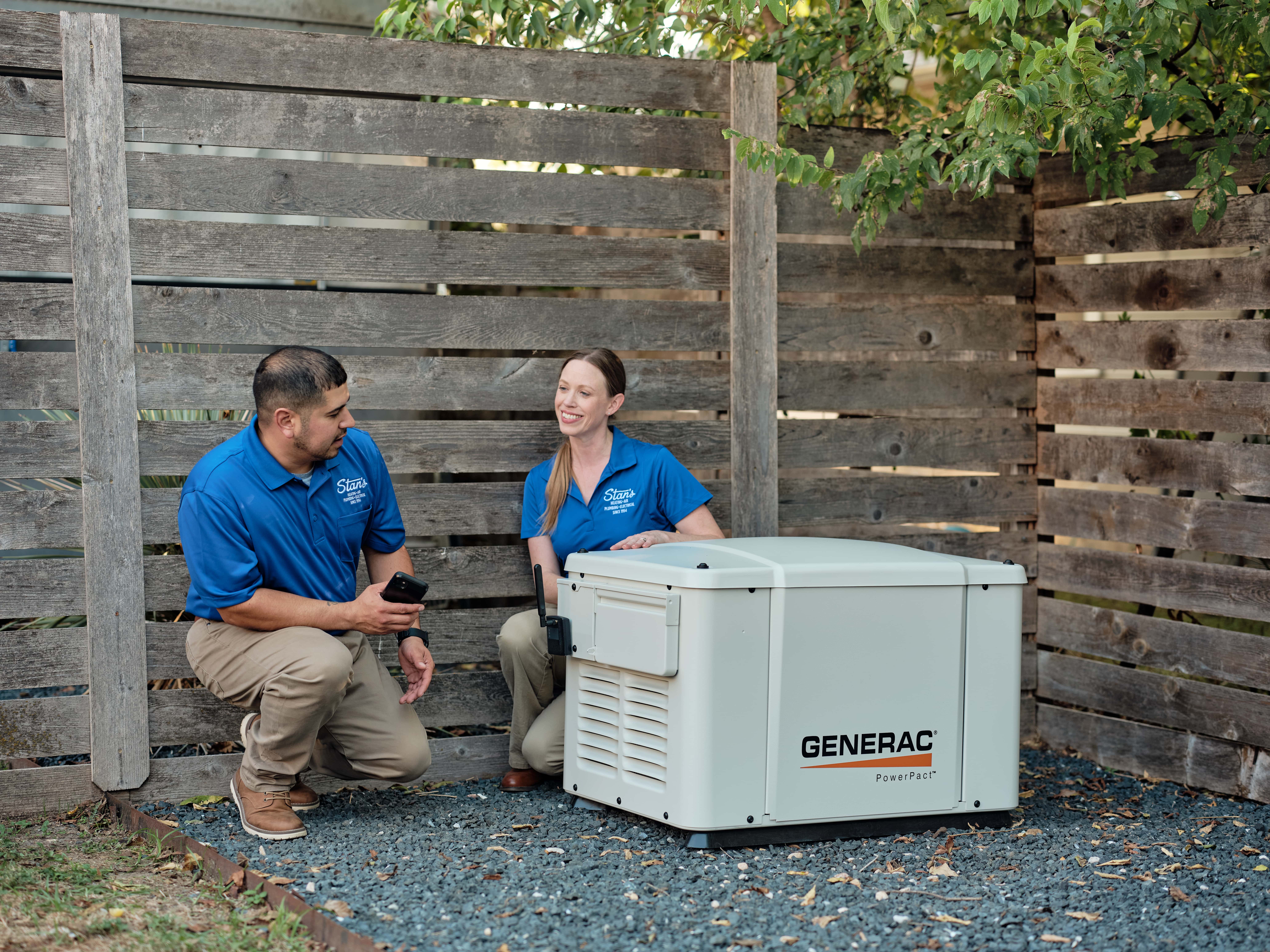 Two technicians in blue shirts next to a Generac generator.