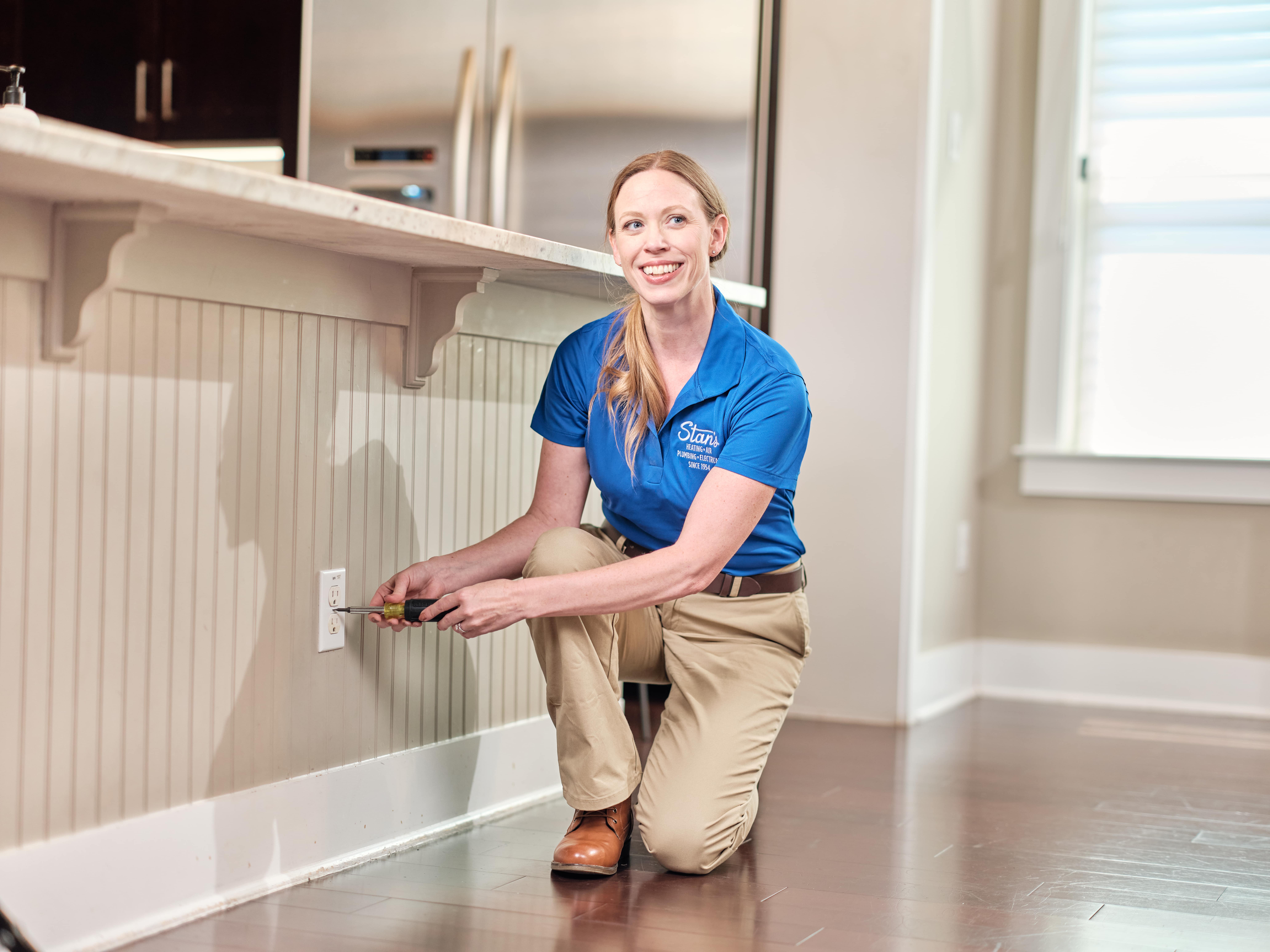 Female technician fixing electrical outlet in kitchen.
