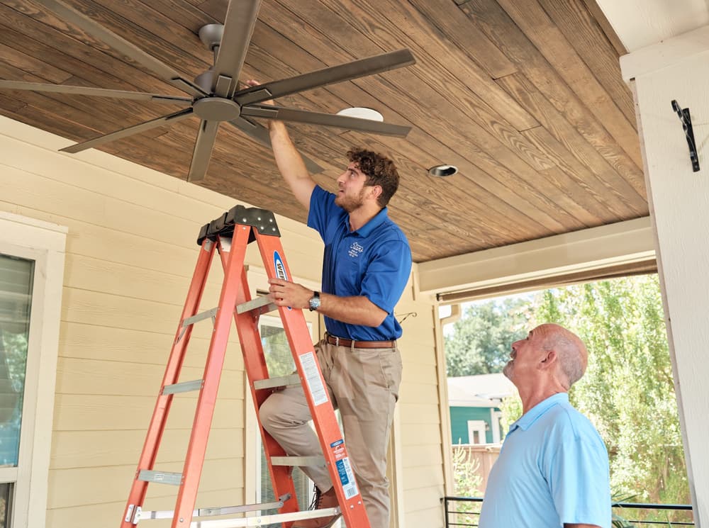 Technician on ladder fixing ceiling fan.