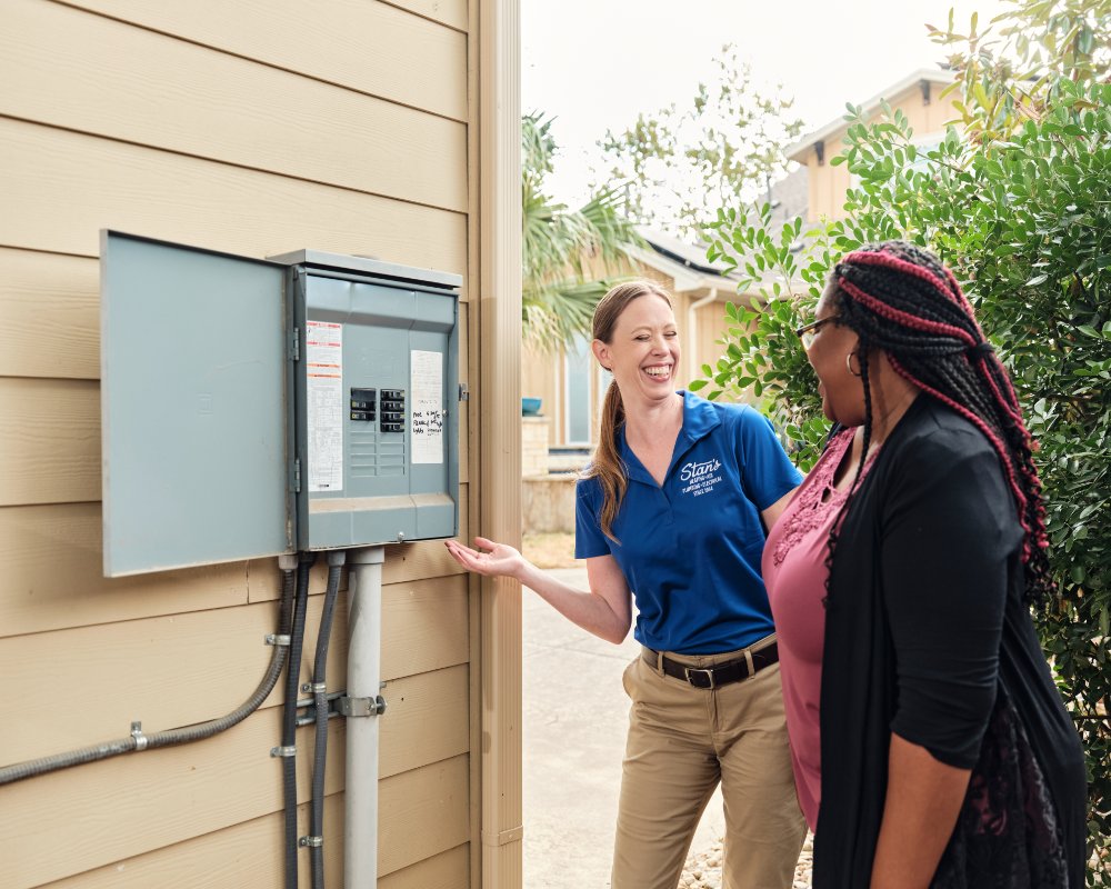 Woman in Stan's HVAC uniform showing customer an electrical panel.
