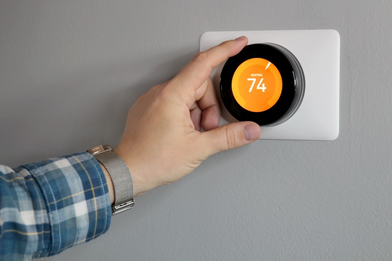 Hand adjusting smart thermostat to 74°.