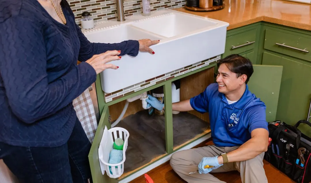 Plumber fixing kitchen sink with homeowner.
