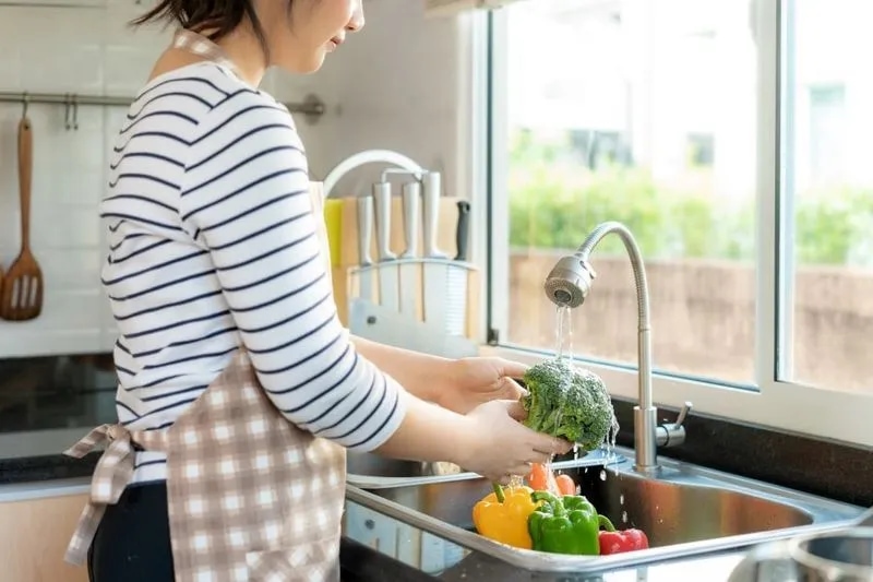 A person washing vegetables in a kitchen sink.
