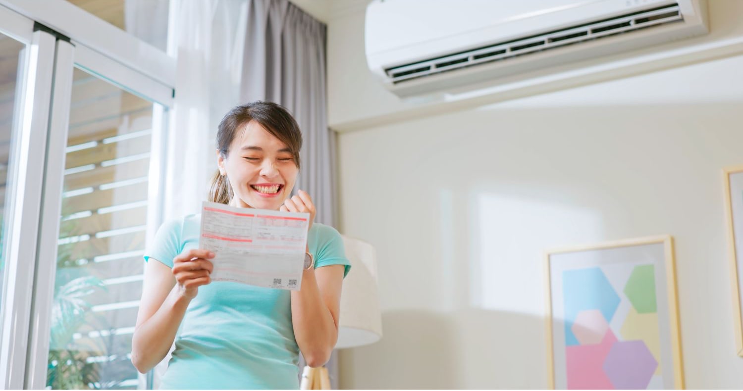 Woman smiling at energy bill under AC unit.