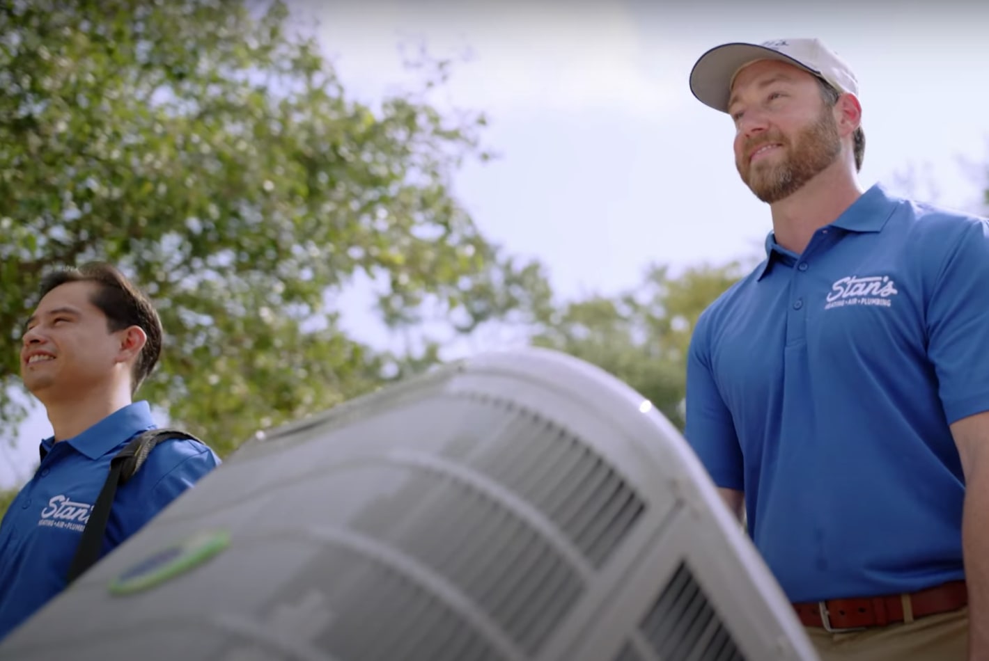 Two Stan's HVAC technicians moving an air conditioner outdoors.