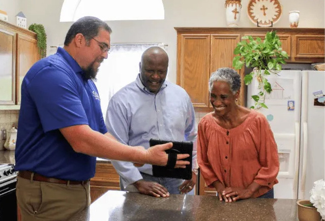 Technician showing AC savings plan to couple in kitchen.