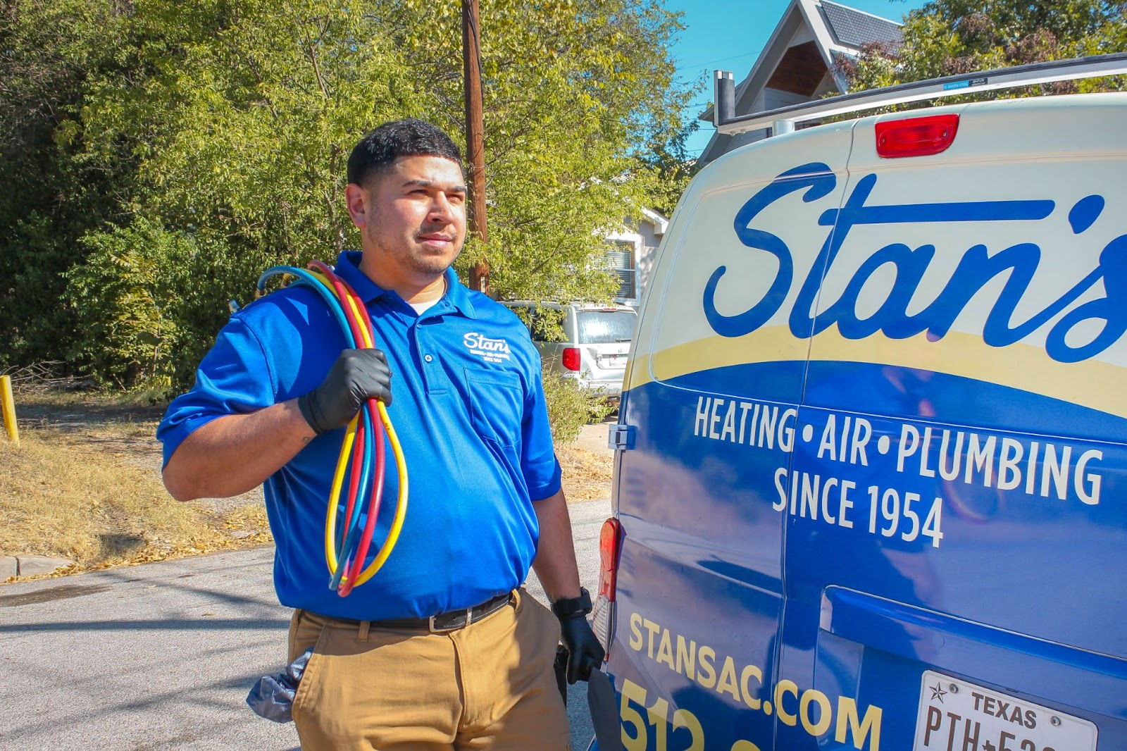 Stan’s Heating, Air & Plumbing technician walking toward a home with tools in hand, with a company service van parked next to him.