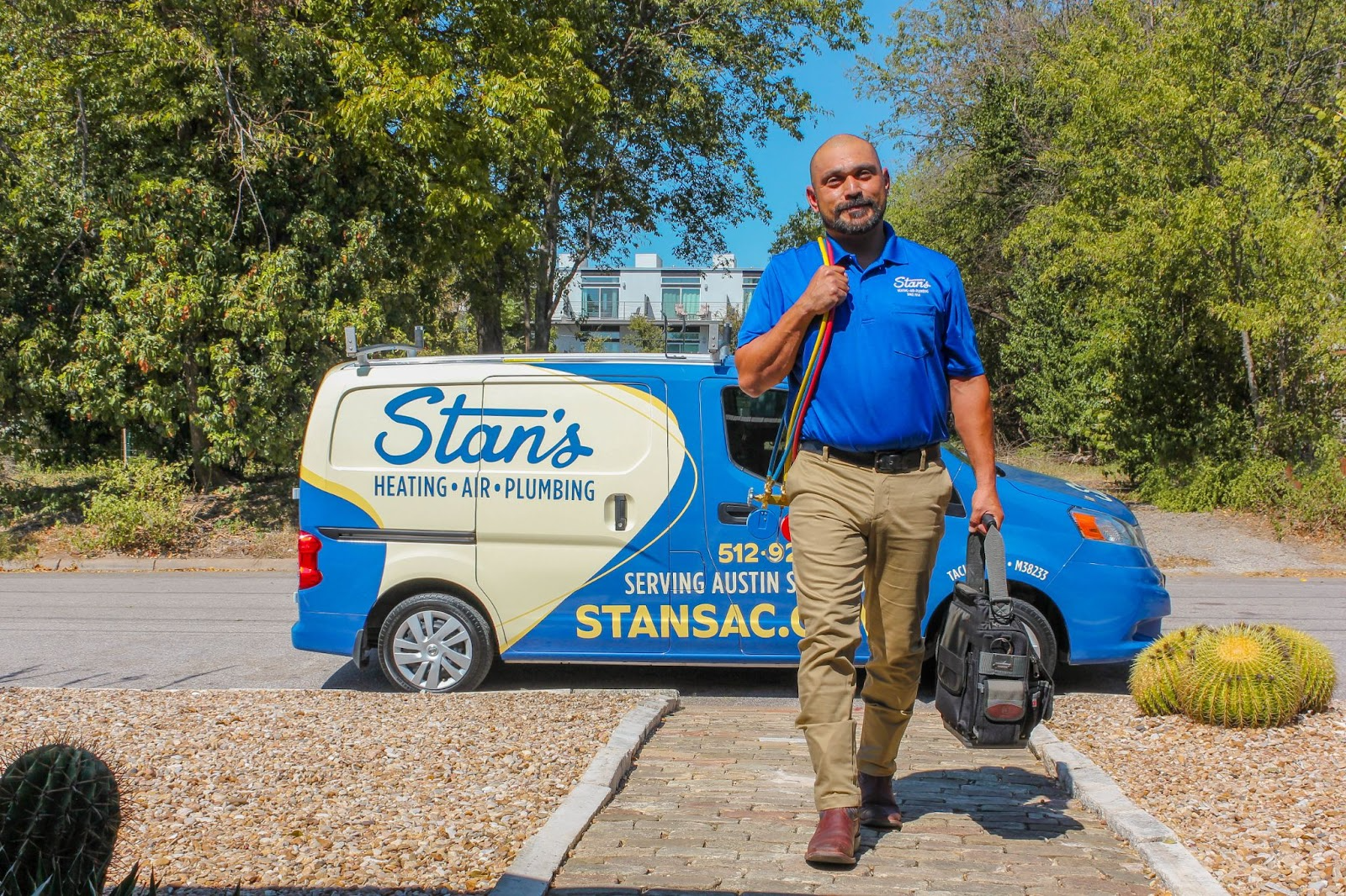 Stan’s Heating, Air, Plumbing & Electrical technician walking toward a home with tools in hand, with a company service van parked behind him