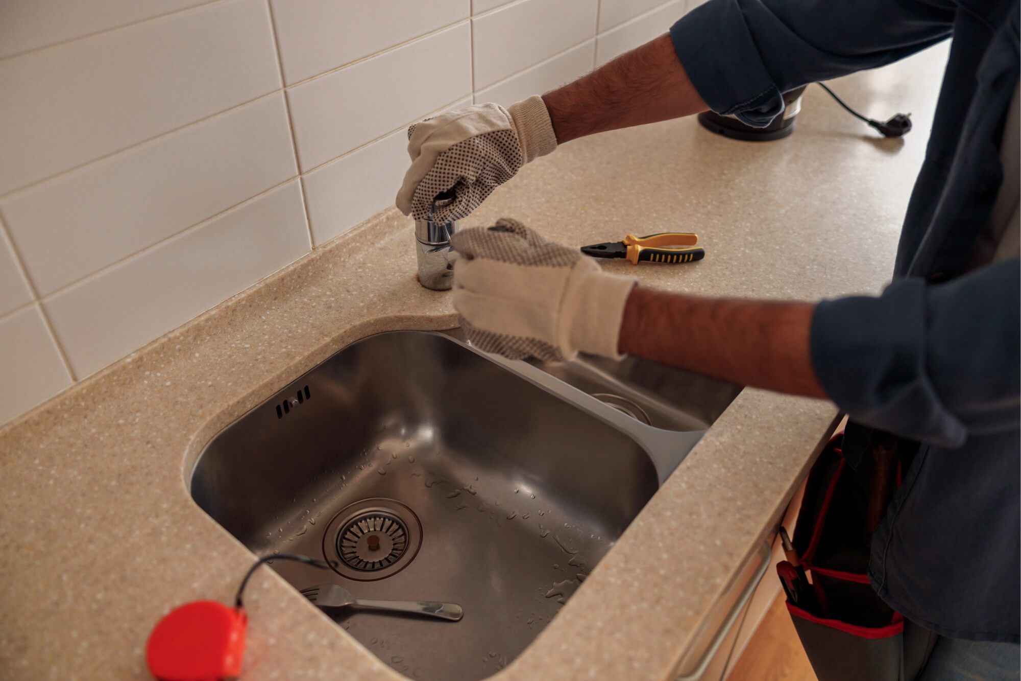 Plumber repairing kitchen sink faucet with tools on countertop.