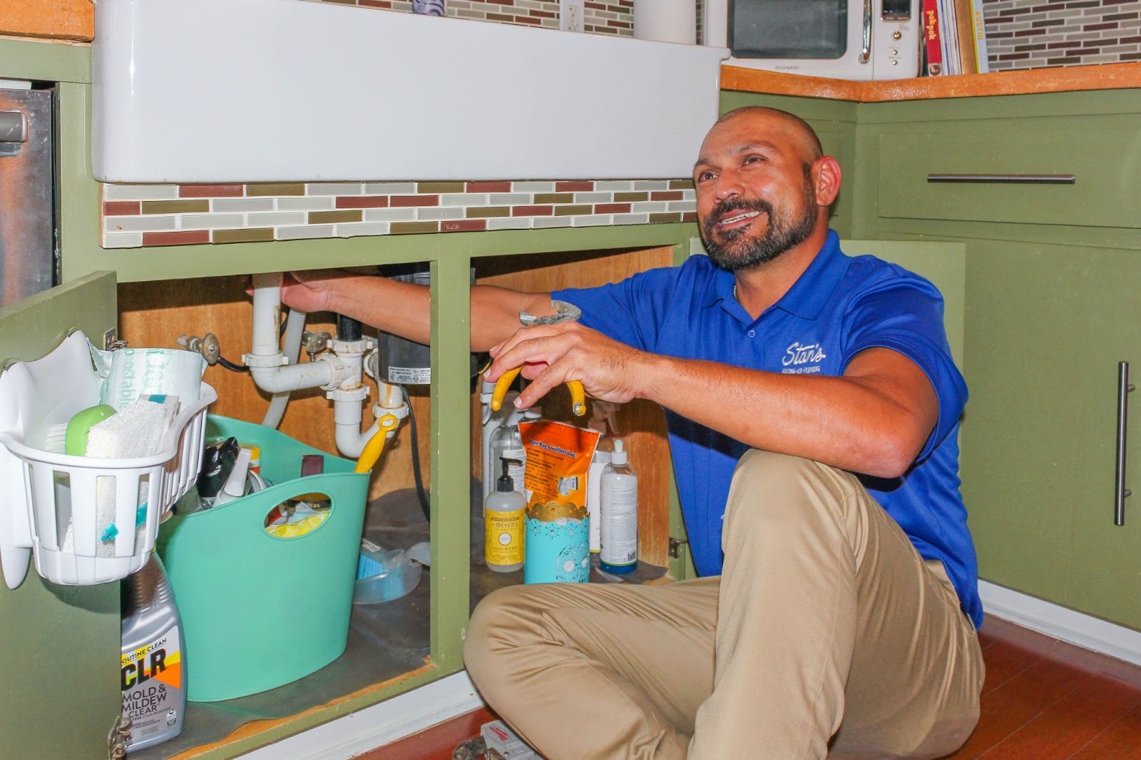 Stan’s plumber is working under a kitchen sink to repair plumbing connections