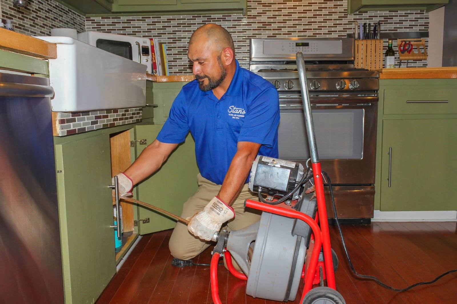 Stan’s plumber using a drain snake machine to unclog a kitchen sink pipe.