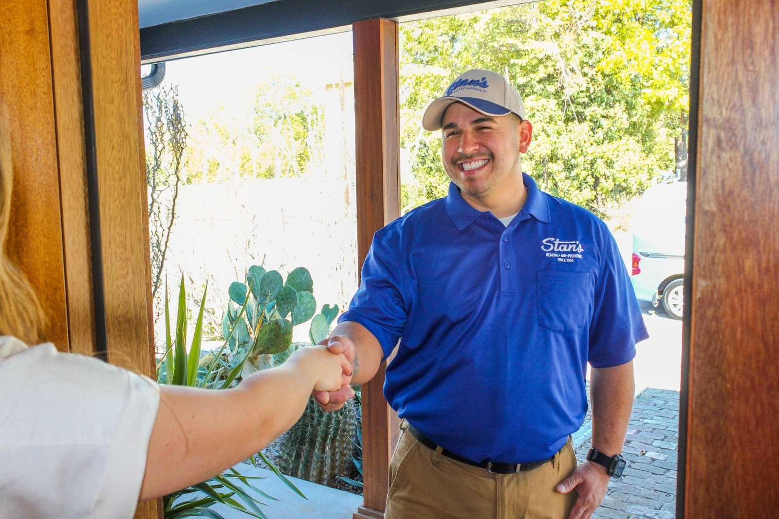Smiling technician from Stan’s Heating, Air & Plumbing shaking hands with a homeowner at the front door.