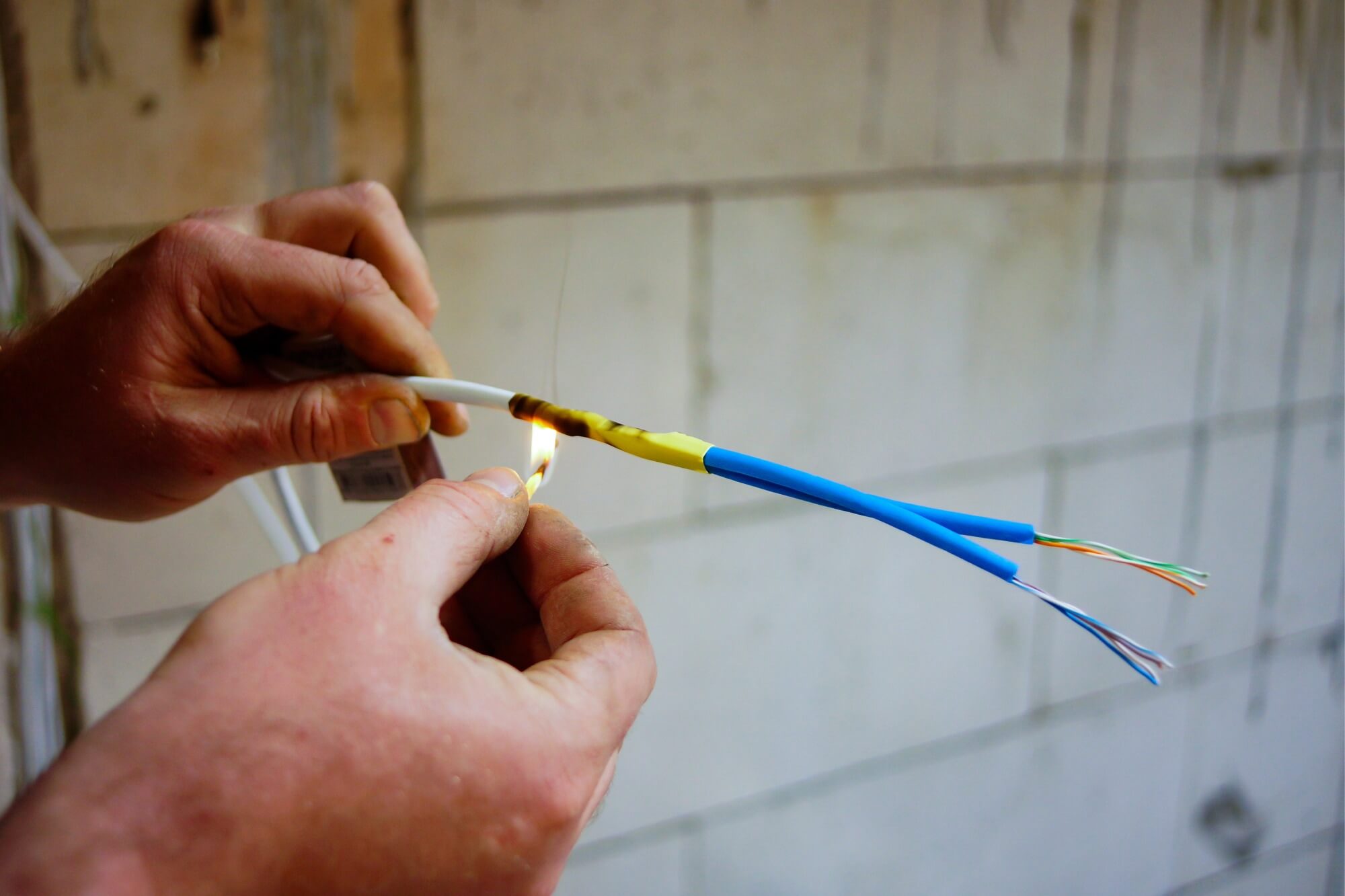 Hands repairing electrical wires against a concrete wall background.