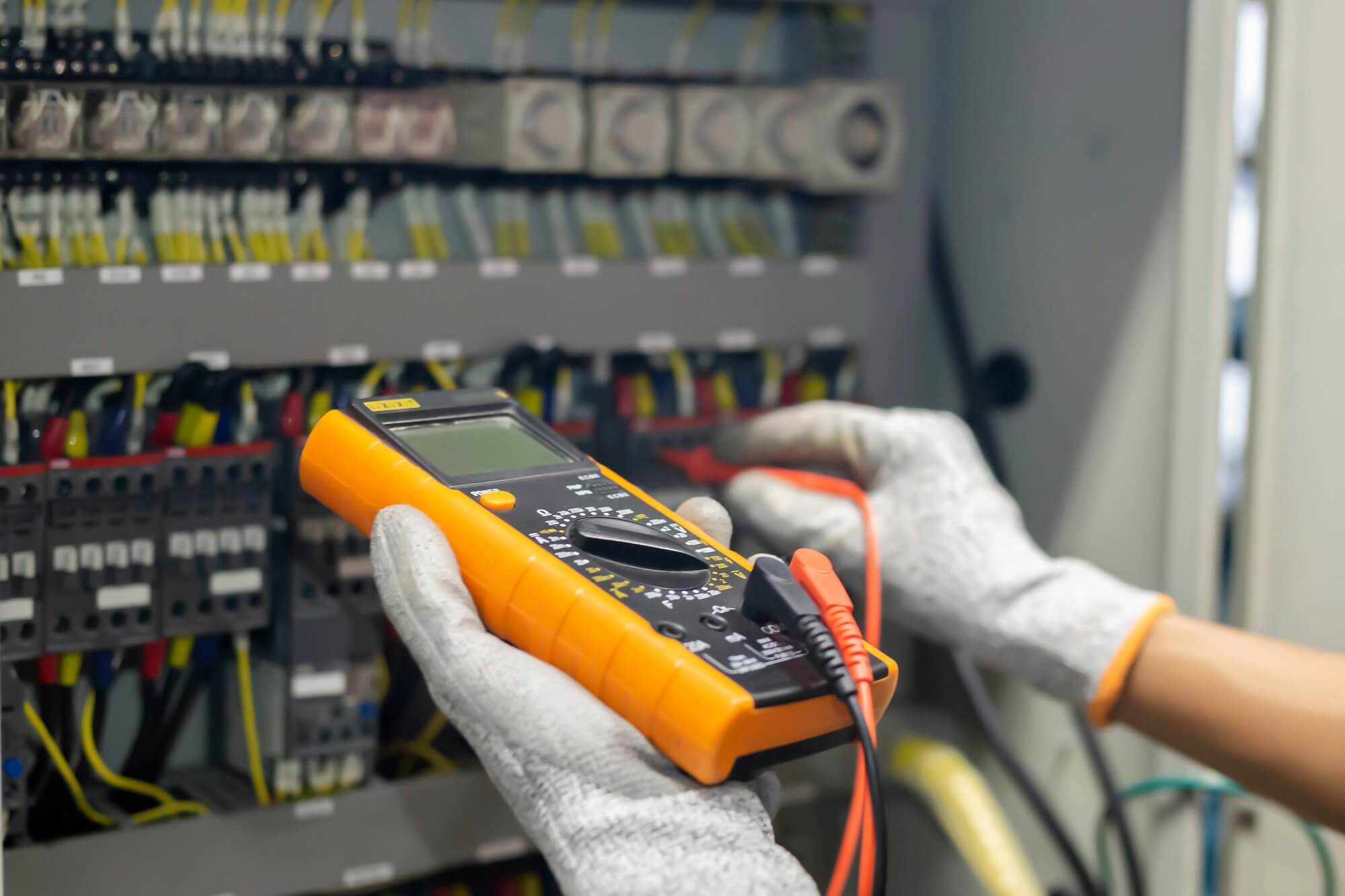 Technician using a digital multimeter to check electrical panel for maintenance and troubleshooting.