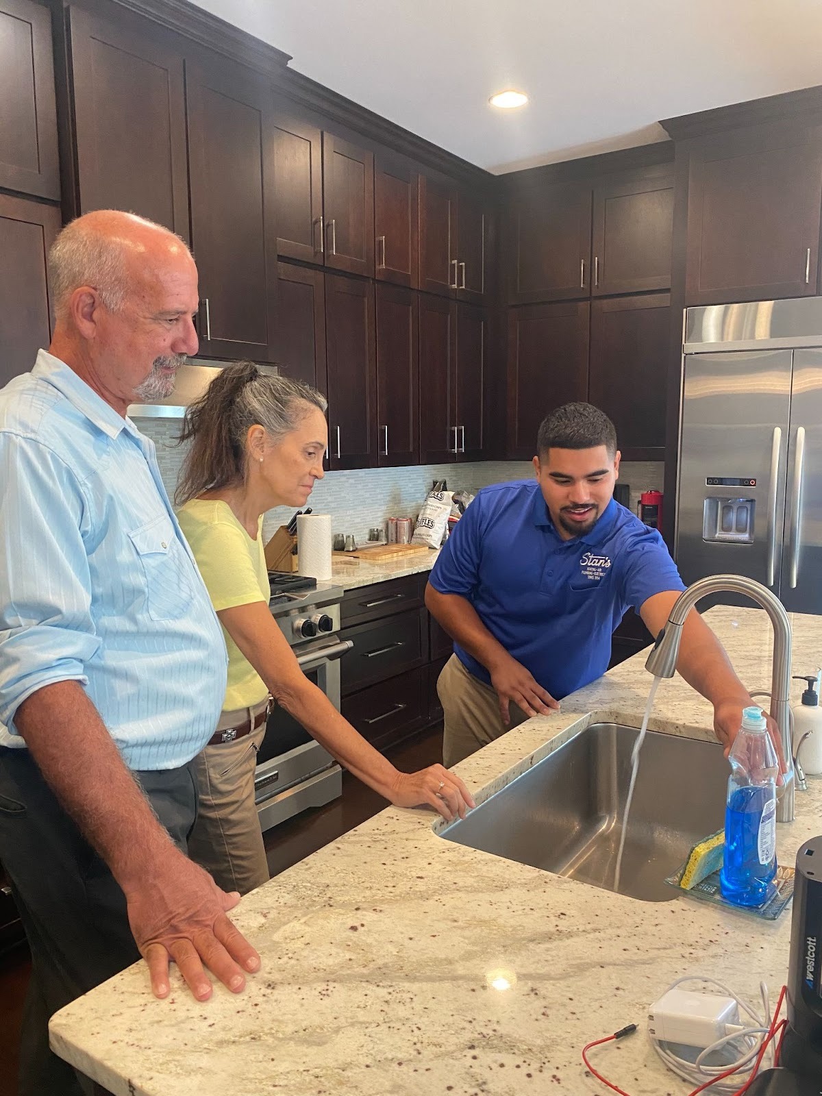 Technician in a blue Stan’s shirt demonstrating a working kitchen faucet to homeowners.
