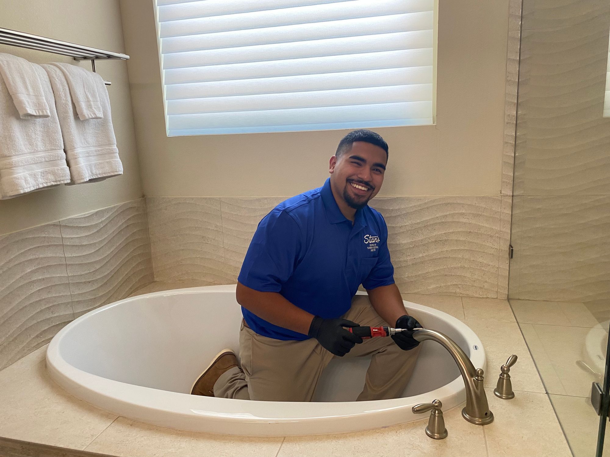 Plumber fixing a bathtub faucet in a modern bathroom, smiling while using a wrench.
