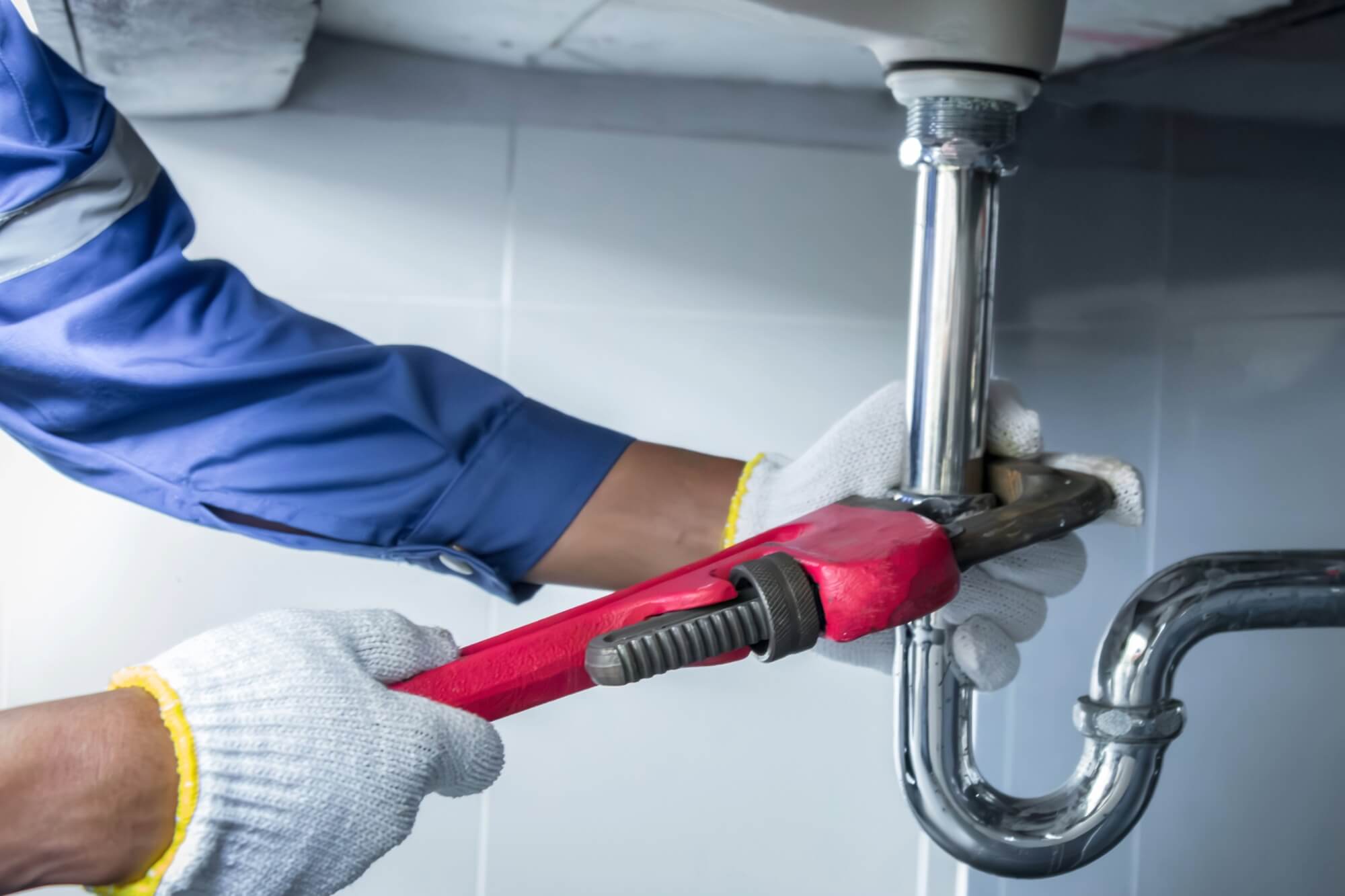 Plumber hands tightening the seal on a sink under the counter with a pipe wrench