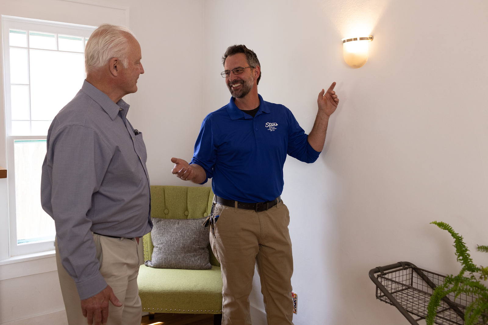 Alt img txt: Technician in a blue Stan’s shirt explaining an indoor wall light fixture to a homeowner.
