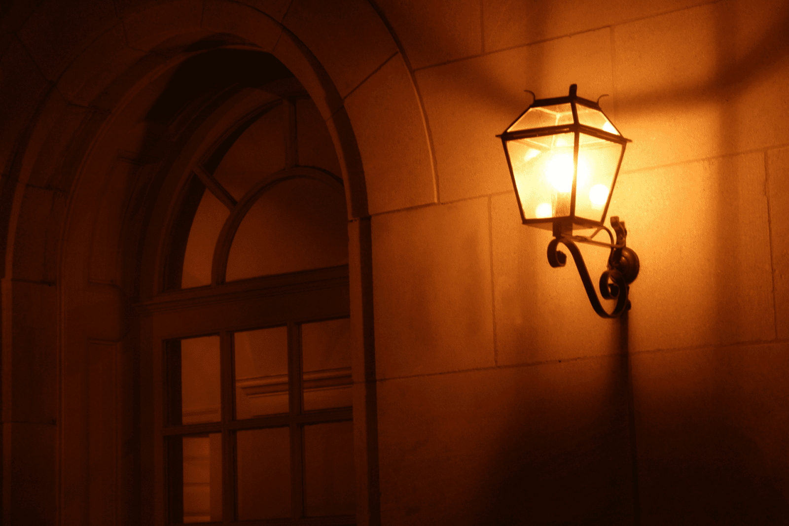 Vintage wall lantern glowing beside an arched doorway at night.