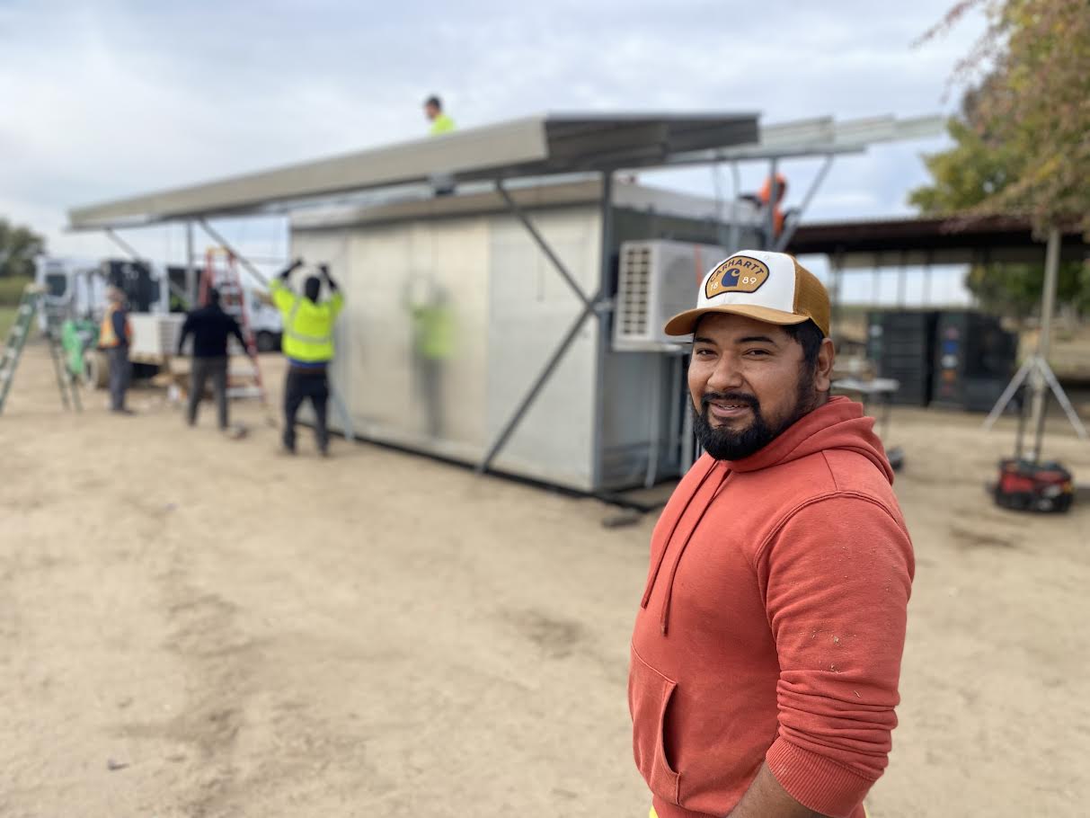 SolarFresco recipient stands smiling in front of a cooler being installed