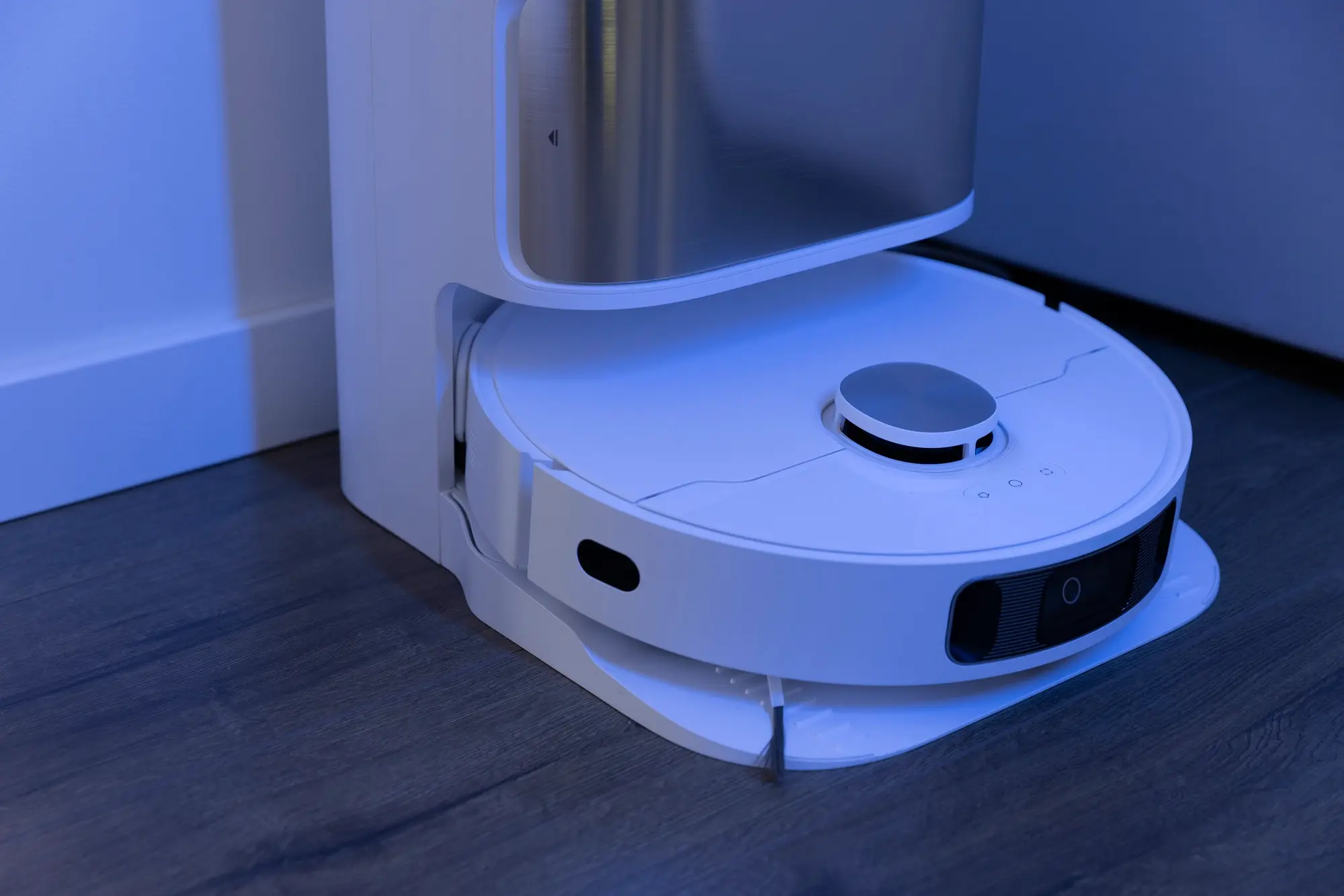 Smart robot vacuum docked in its charging station on a hardwood floor, representing the convenience and automation of modern home cleaning technology.