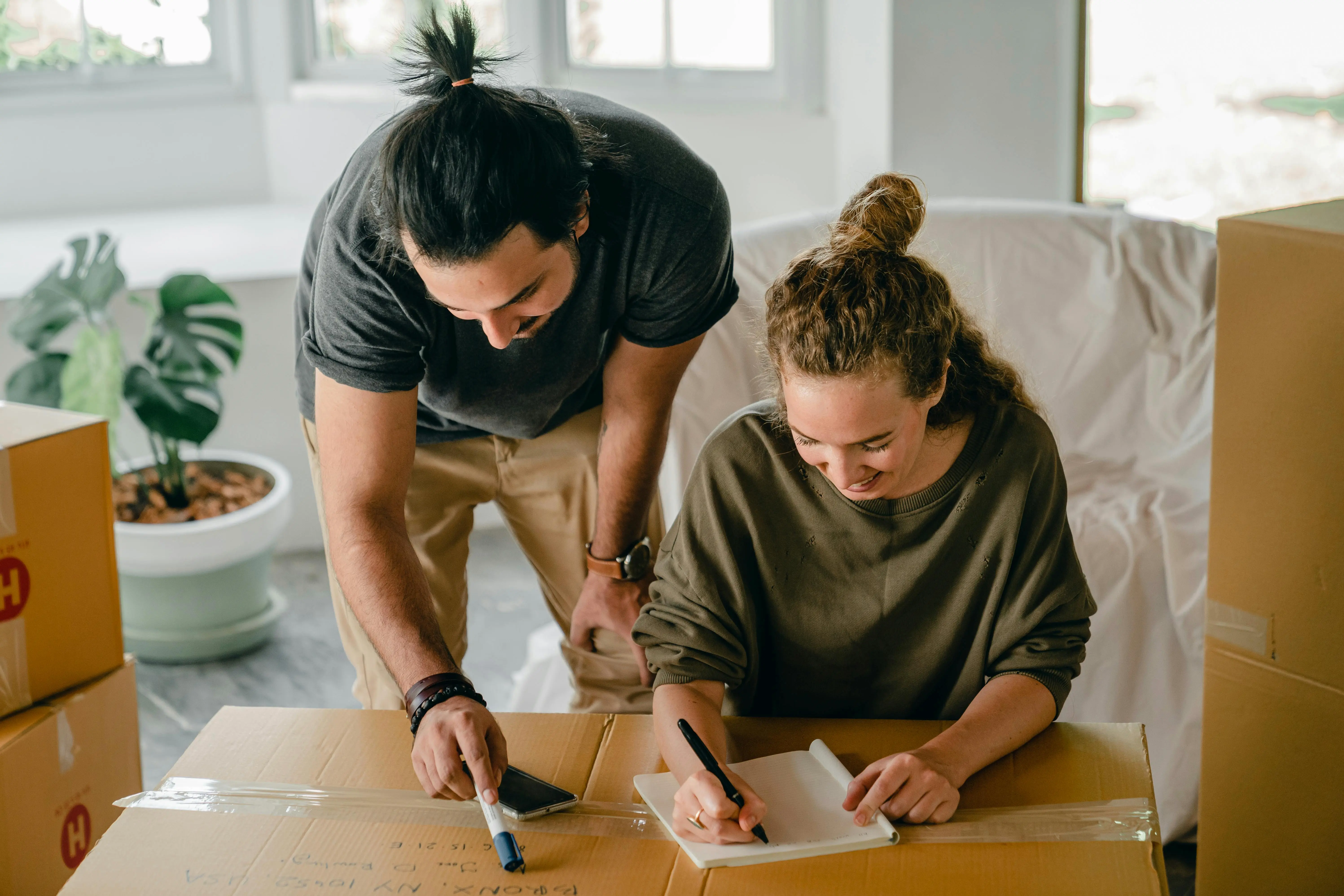 Couple reviewing a checklist together while unpacking moving boxes in a bright living room, representing Toronto home sellers preparing for a pre-listing cleaning plan.