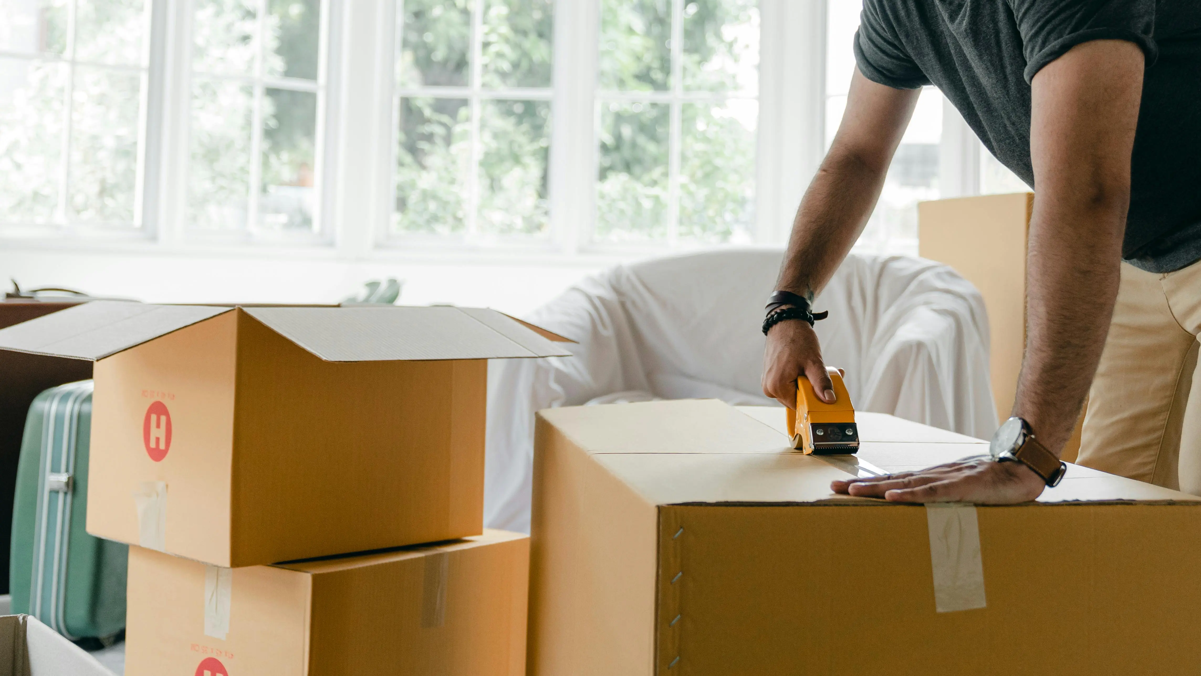 Person sealing cardboard moving boxes in a bright room, illustrating organized storage spaces for Toronto home staging.