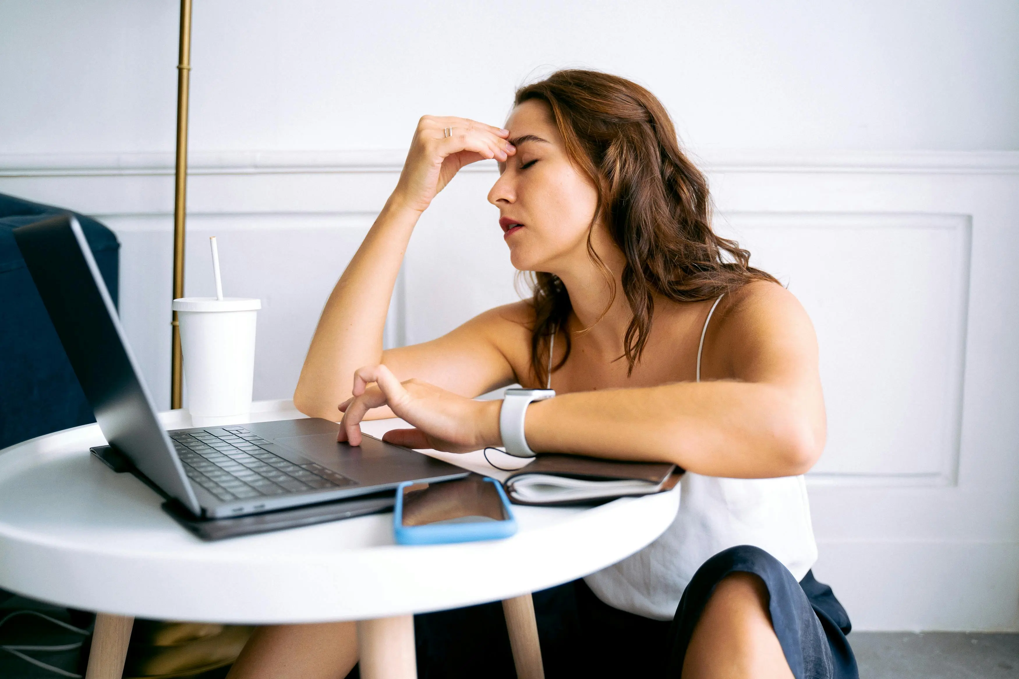 Stressed woman sitting at a desk with a laptop, holding her head in frustration, representing the feeling of being chronically overwhelmed by cleaning tasks.