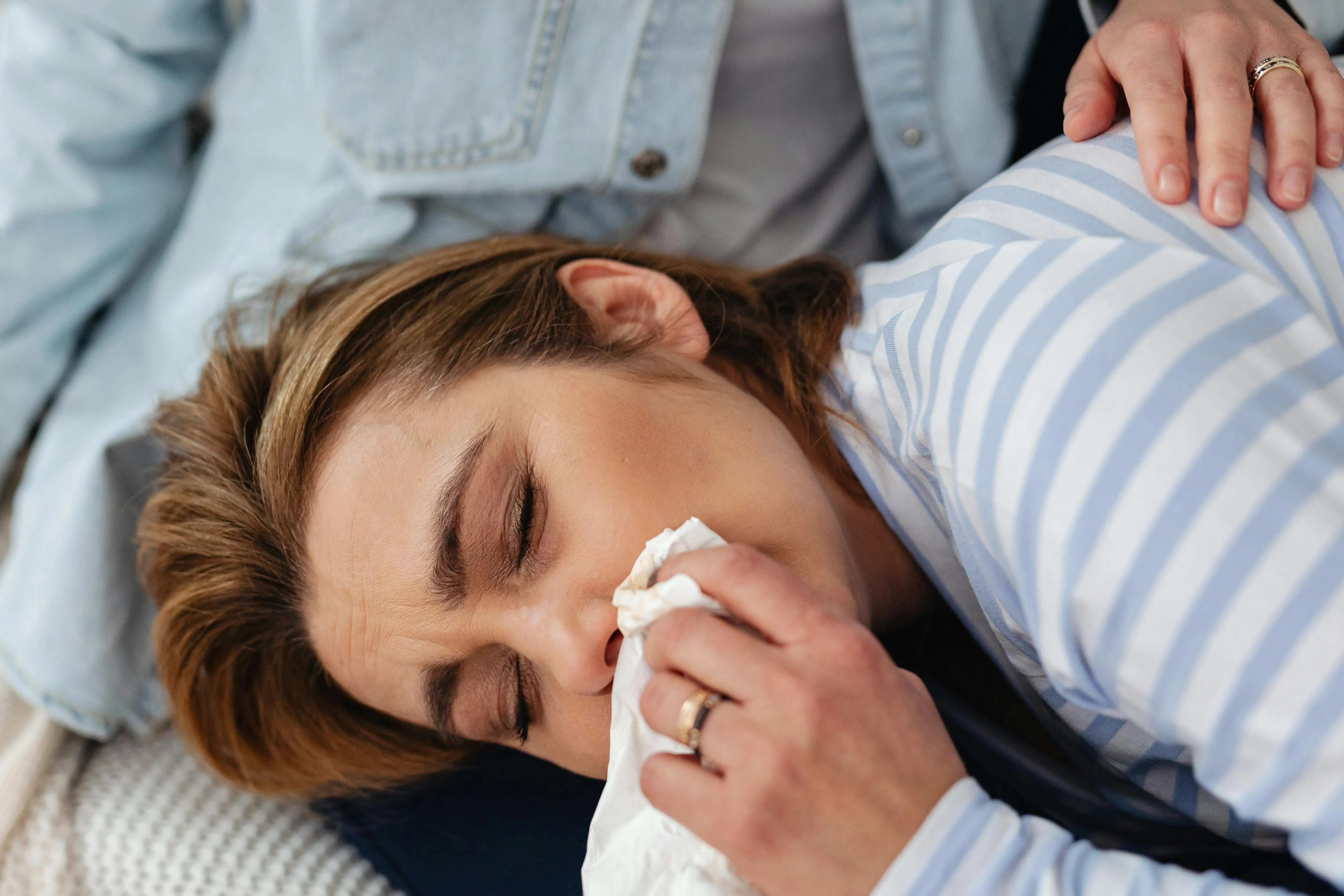 Woman lying on a couch using a tissue to blow her nose, illustrating allergies and poor air quality as signs a home may need professional cleaning.